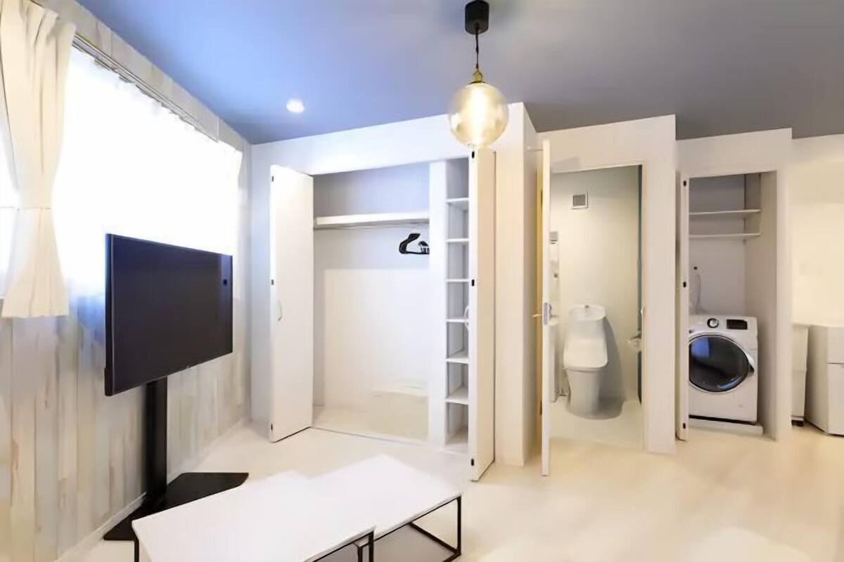 A modern, well-lit room with a flat-screen TV, a table, a built-in wardrobe, and a washing machine.