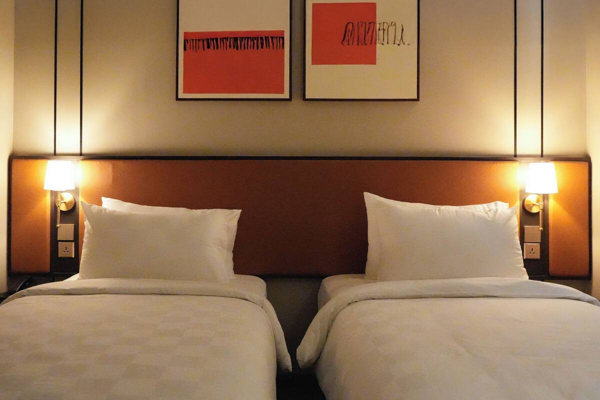 Une chambre d’hôtel avec deux lits, chacun étant équipé de draps et d’oreillers blancs. Deux lampes murales sont fixées de part et d’autre des lits.