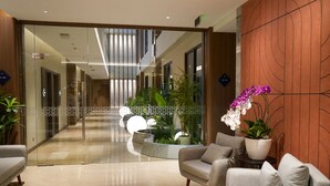 Un hall d’entrée moderne avec une cloison en verre, un espace détente avec des canapés et des plantes en pot.