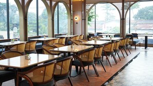 Un restaurant doté de nombreuses tables et chaises, de grandes fenêtres et offrant une vue sur la verdure environnante.