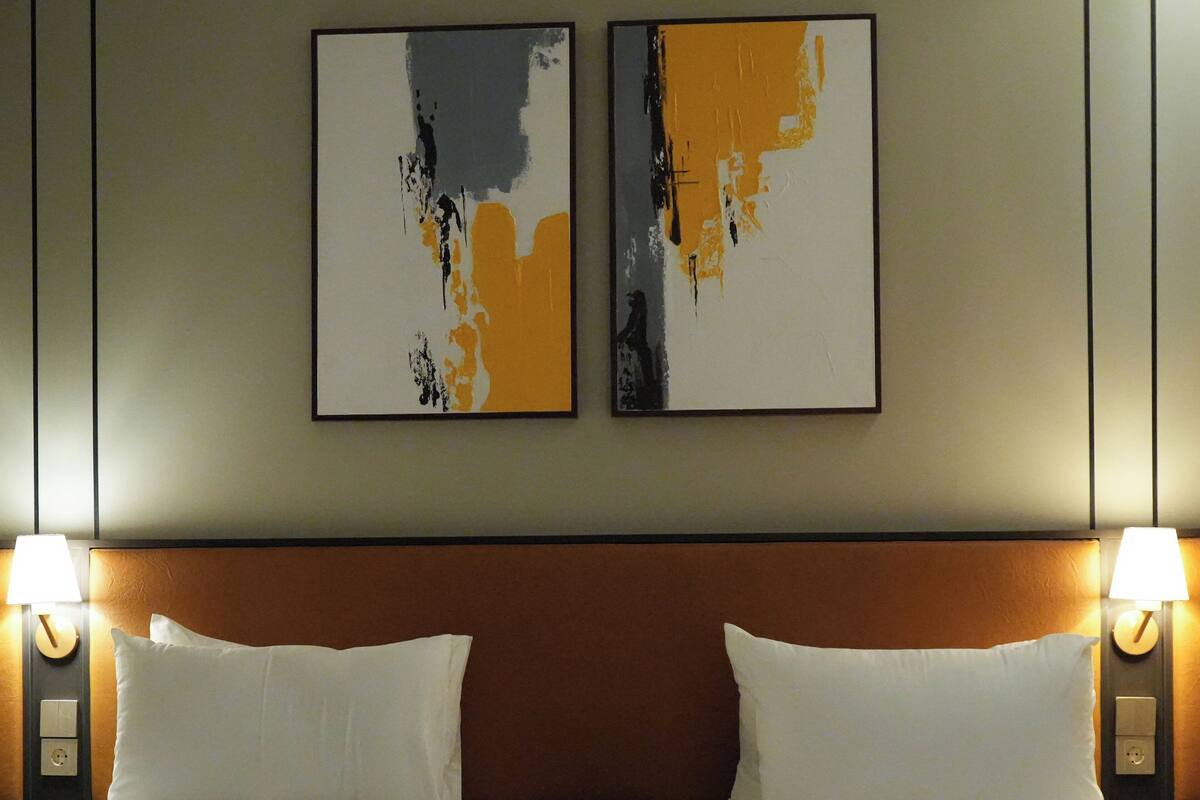 Une chambre d’hôtel avec deux lits, une tête de lit en bois et deux lampes fixées au mur.