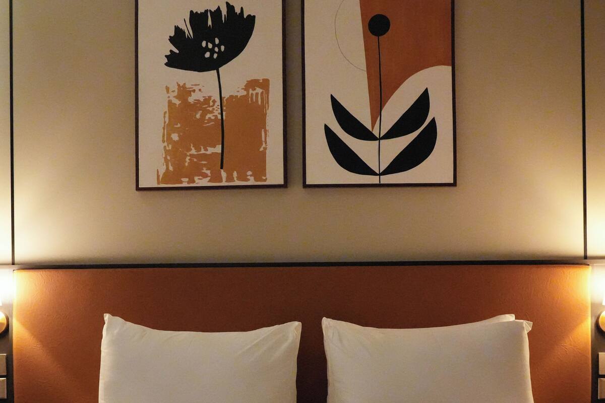 Une chambre d’hôtel avec un grand lit, deux oreillers et deux œuvres d’art fixées au mur, représentant des motifs floraux abstraits.