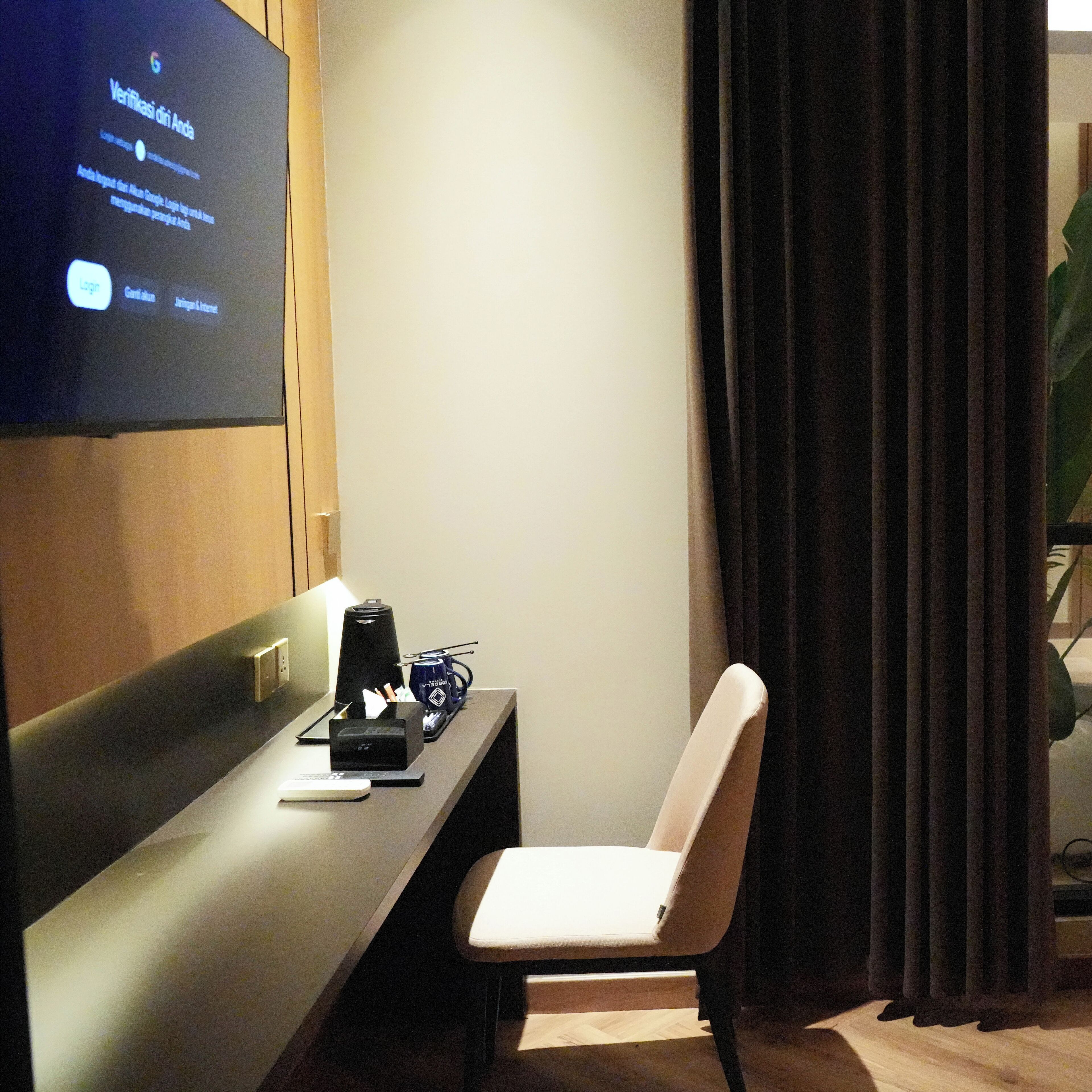 Ein Hotelzimmer mit einem an der Wand befestigten Flachbildfernseher, der einen Verifikationsbildschirm anzeigt, einem Schreibtisch mit Kaffeemaschine, einem Laptop und einem Stuhl.