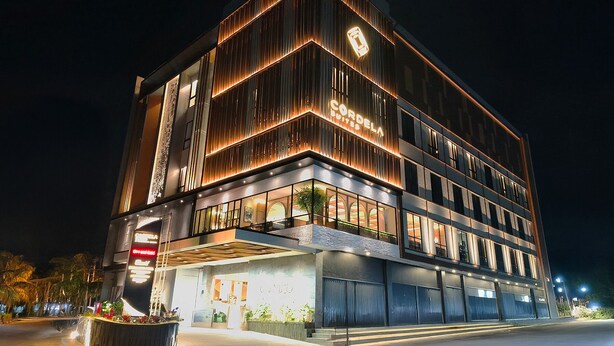 Un hôtel moderne, reconnaissable à son grand panneau « CORDELA », qui s’étend sur plusieurs étages et dont la façade est bien éclairée.