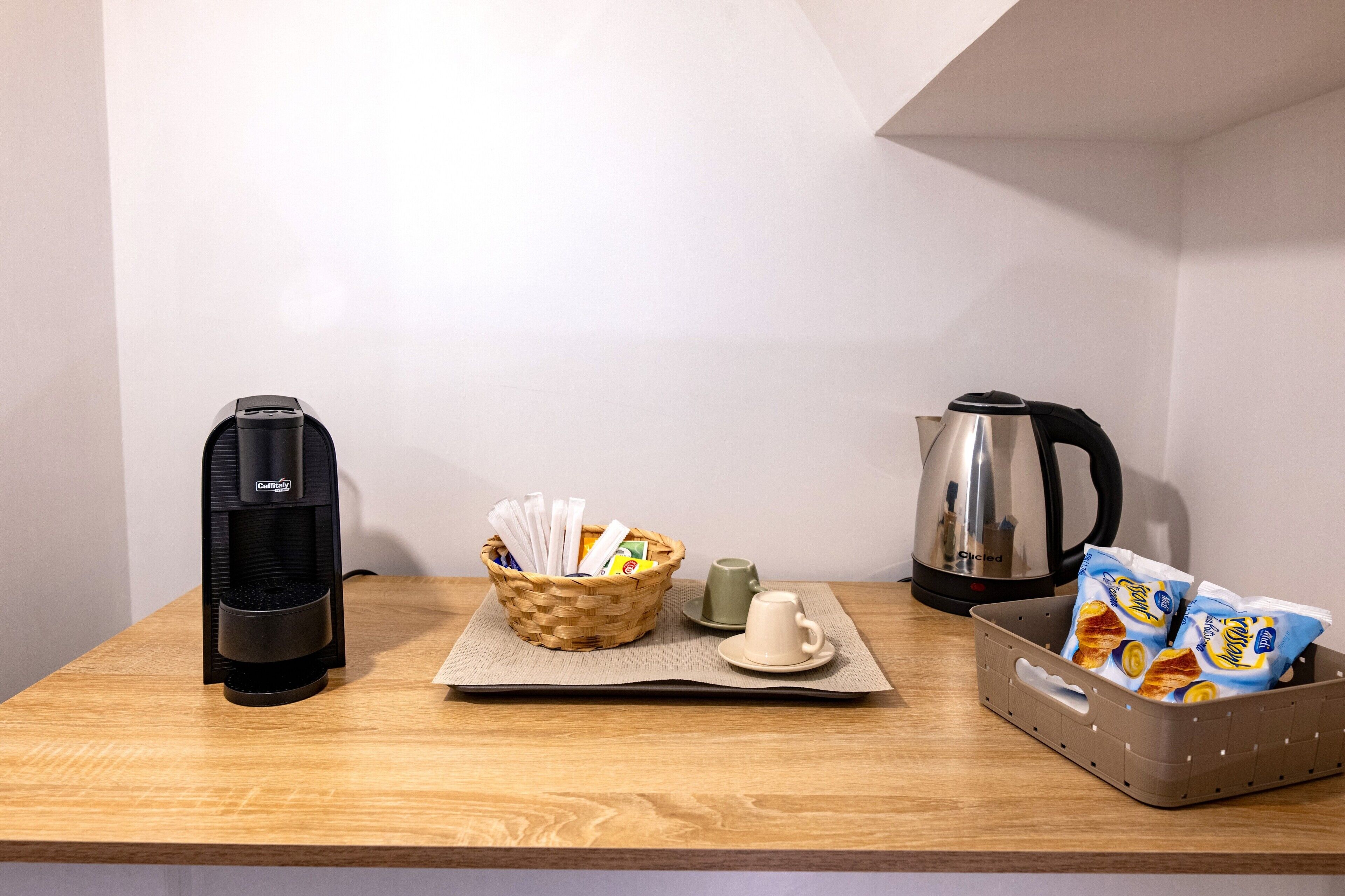 A wooden table with a coffee maker, a basket with snacks, a teapot, and a cup.