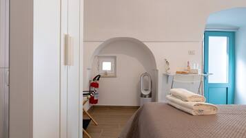A hotel room with a bed, a towel rack, a fire extinguisher, a mirror, and a blue door.