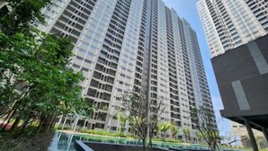 A high-rise residential building with multiple balconies, surrounded by greenery and a swimming pool.