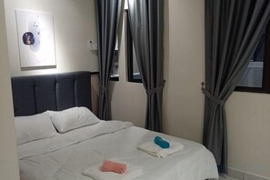 A bedroom with a bed, curtains, a wall-mounted light switch, and a framed picture.
