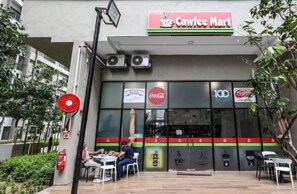 A Cawfee Mart with a Coca-Cola and 100 logo on the facade, outdoor seating, and a fire extinguisher. - Nilai Youth City Residence C-25-15 (Nilai)