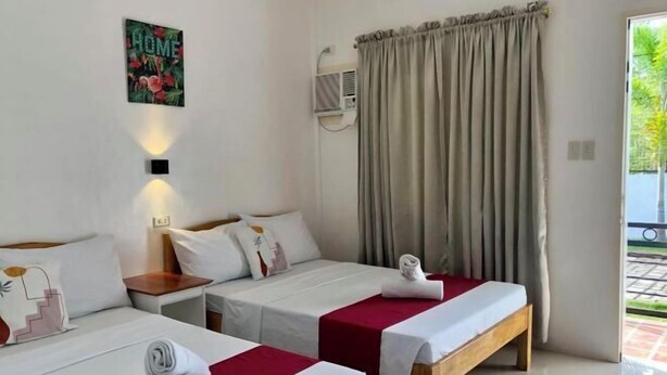 A hotel room with two beds, a 'HOME' sign, an air conditioning unit, and a view of the outside. - Sunshine Stay Panglao (Panglao)