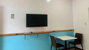 A room with a flat-screen TV mounted on the wall, a wooden counter, a white table, and two chairs. - Sunshine Stay Panglao (Panglao)