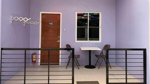 A room with a purple wall, a wooden door, a window, a small table, two chairs, and a fire extinguisher. - Sunshine Stay Panglao (Panglao)