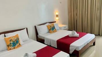Dos camas individuales con ropa de cama blanca y roja, una mesita de noche, una lámpara de pared y una ventana con cortinas.