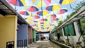 A corridor with colorful umbrellas hanging from the ceiling, a tiled floor, and potted plants along the walls. - Sunshine Stay Panglao (Panglao)