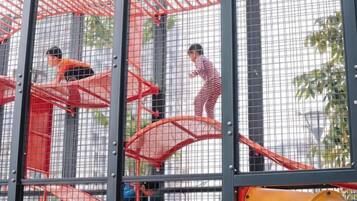 A playground structure with multiple levels and enclosed areas, surrounded by a safety net.