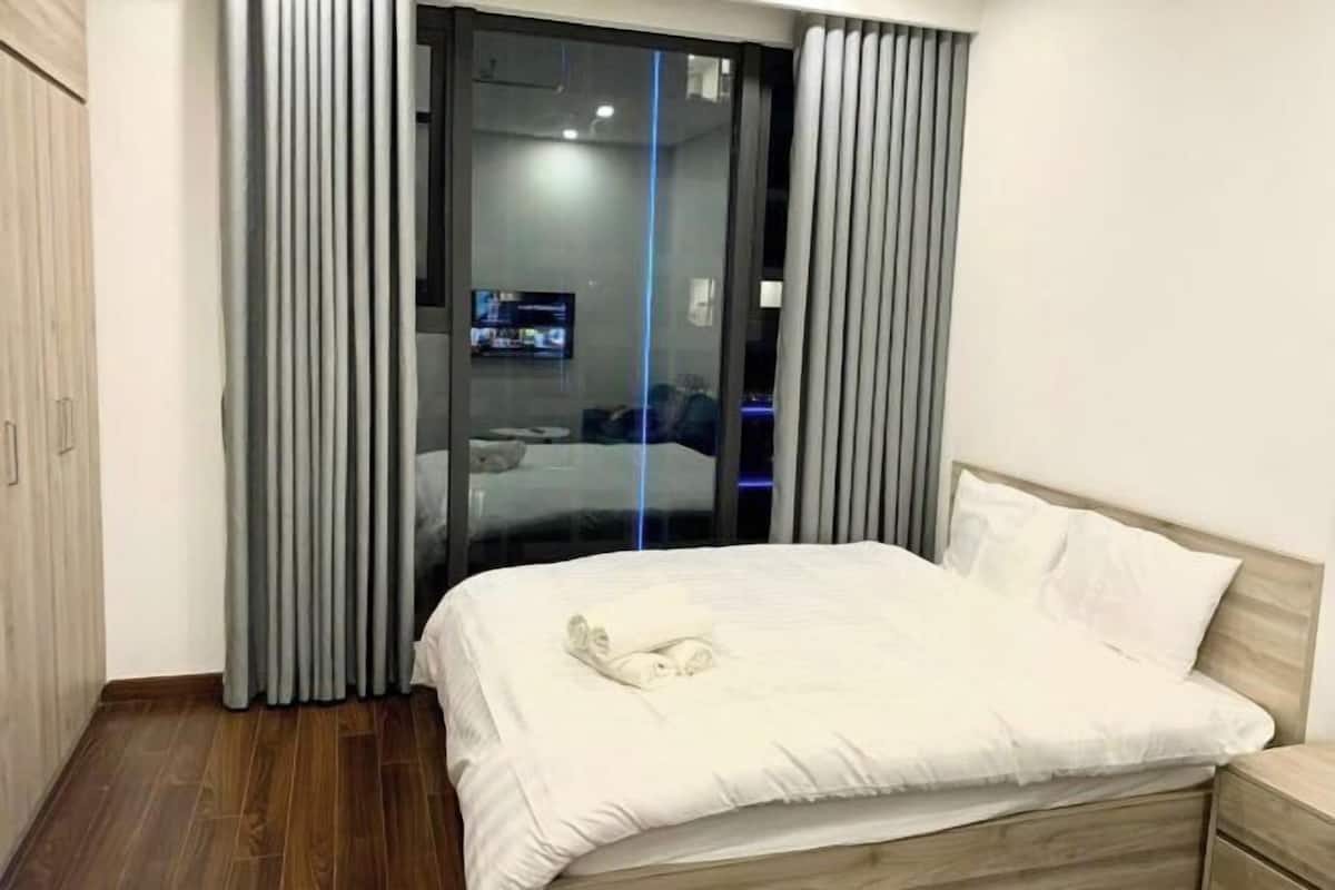 Ein modernes Schlafzimmer mit einem großen Bett, einem Nachttisch aus Holz und einer Schiebeglastür zum Badezimmer.