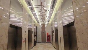 A modern elevator lobby with marble floors and walls, a person standing near the elevators, and a red emergency phone. - LISA HOUSE - MASTERI WEST HEIGHTS - VINHOMES SMART CITY (Hanoi)
