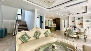 A spacious living area with a sofa, a dining table, and chairs. There is a staircase in the background leading to another level.
