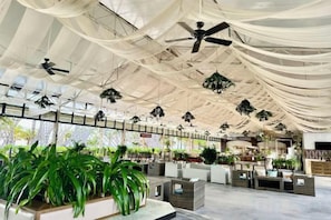 Un espace intérieur vaste et aéré, doté de ventilateurs de plafond, de plantes suspendues et de différents types de sièges.