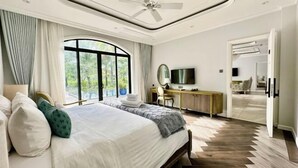A bedroom with a bed, a desk, a television, and a view of the outdoors.
