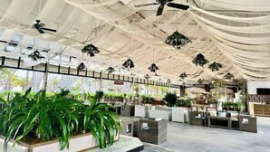A spacious indoor area with ceiling fans, hanging plants, and seating arrangements.