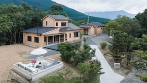 A modern two-story house with a large patio area, surrounded by lush greenery and mountains. - SEN.RETREAT TAKAHARA (Tanabe)