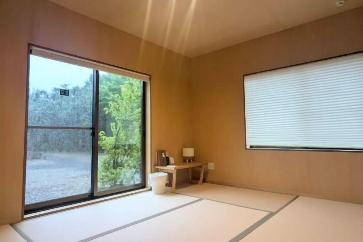 A room with tatami flooring, a sliding door, a small table with a lamp, and a window with blinds.
