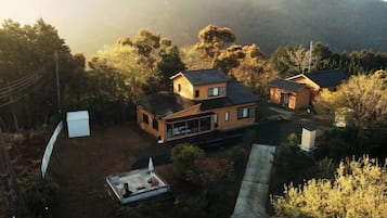 A two-story house with a large backyard, surrounded by trees and hills.