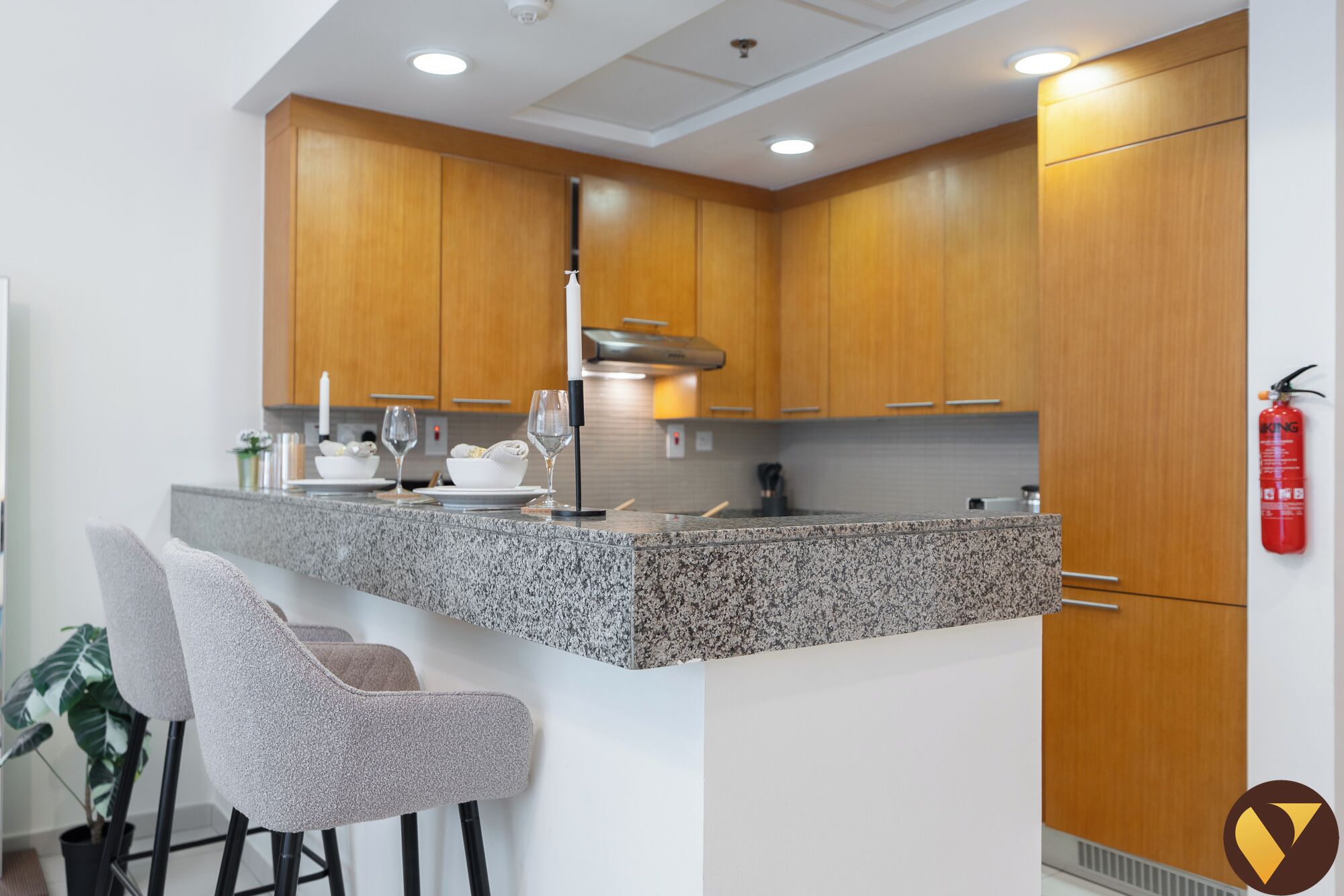 A modern kitchen with granite countertops, wooden cabinets, and a bar area with two chairs.