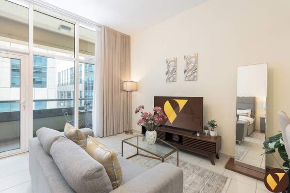 A modern living room with a sofa, coffee table, TV, and artwork. - Vogue | Bay Square Business Bay close to Dubai Mall | Burj Khalifa (Dubai)