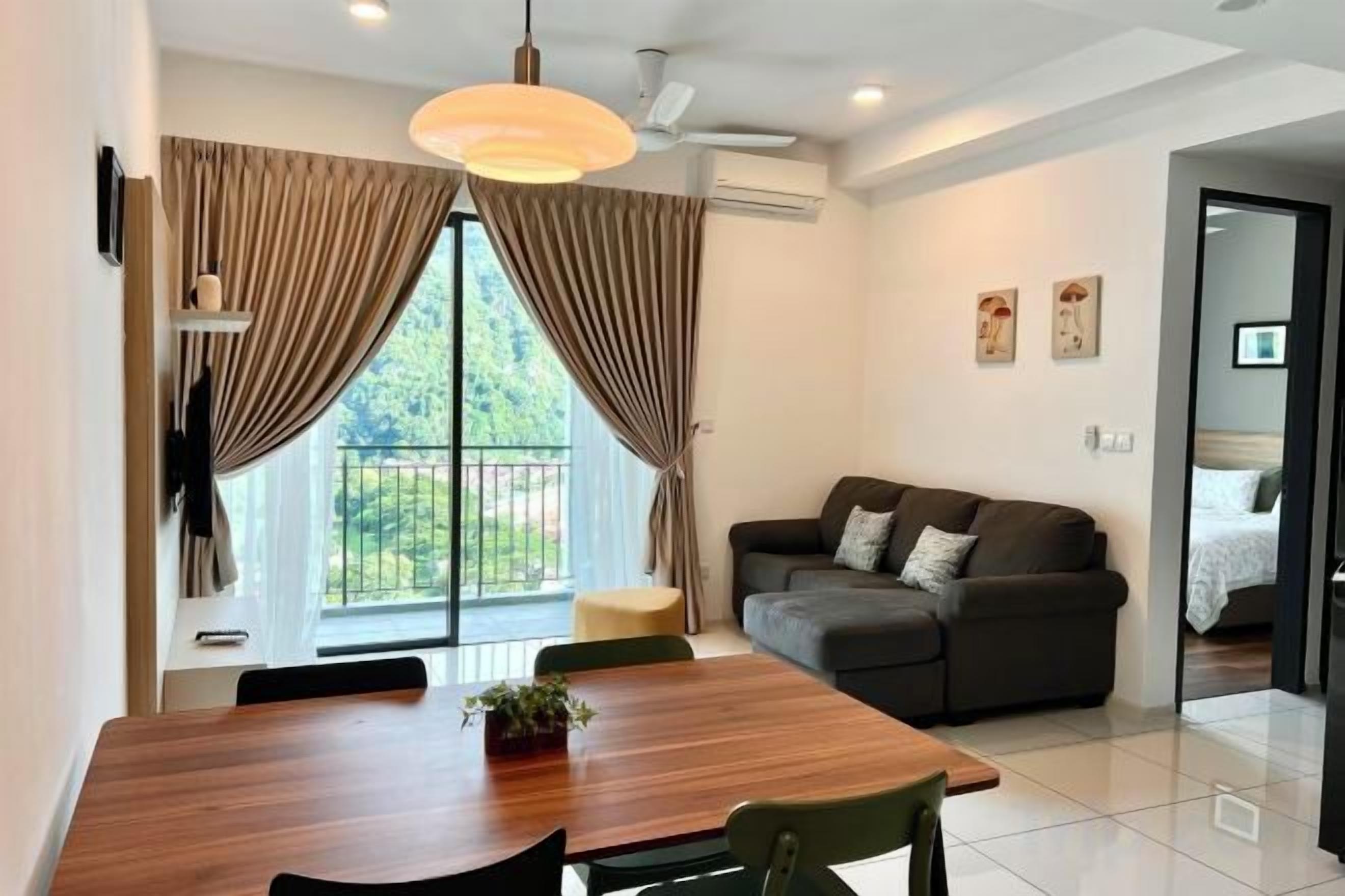 A modern living room with a dark sofa, a wooden dining table, and a large window with curtains.