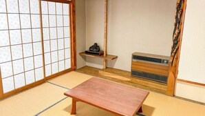 Ein traditioneller japanischer Raum mit Tatami-Böden, einer Schiebetür, einem kleinen Regal mit einem Dekorationsobjekt und einer eingebauten Klimaanlage.