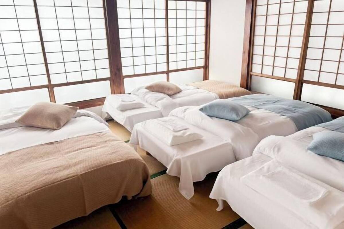 Quarto com três camas dispostas em linha, cada uma com travesseiro e cobertor.