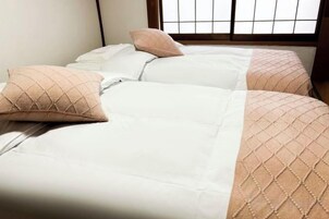 Una habitación de hotel con dos camas, cada una con cubrecama blanco y una sola almohada decorativa.