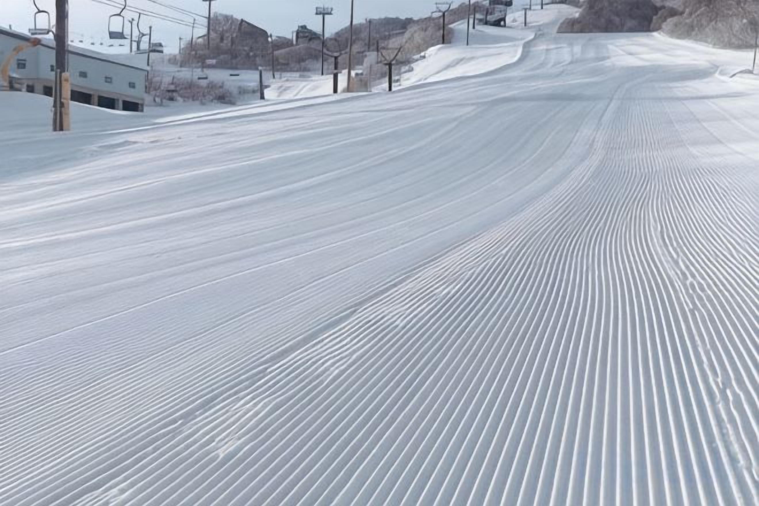 A snow-covered ski slope with ski lifts and buildings in the background.