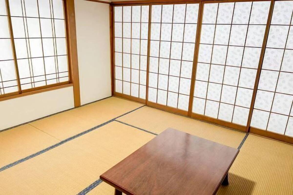 Um espaço com esteiras de tatame, mesa de madeira e painéis shoji.