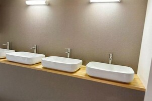 Tres lavamanos blancos y rectangulares sobre una encimera de madera en un baño.