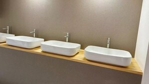 Drei weiße, rechteckige Waschbecken auf einer Holzauslage in einem Badezimmer mit beige gestrichenen Wänden und Beleuchtung unter den Schränken.