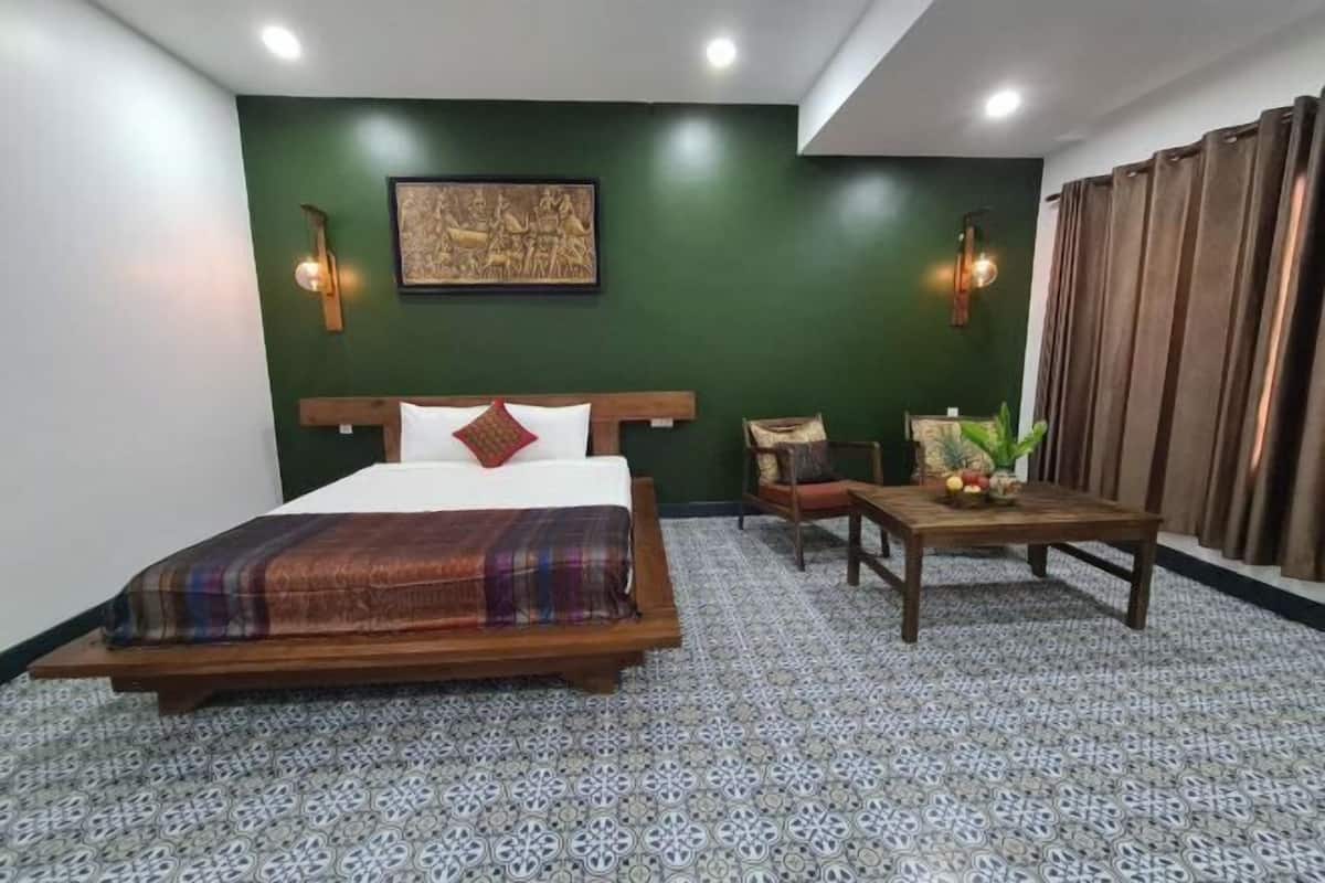 A bedroom with a bed, a table with fruits, a chair, and a wall-mounted light fixture.
