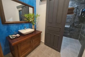 A bathroom with a wooden vanity, a white sink, a mirror, a potted plant, and a shower area. - Villa Romduol (Kampot)