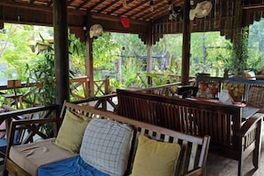 An outdoor wooden deck with seating, surrounded by lush greenery. - Villa Romduol (Kampot)