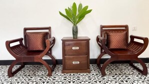 Two wooden chairs with cushioned seats and backs, a small wooden side table with drawers, and a potted plant on the table. - Villa Romduol (Kampot)