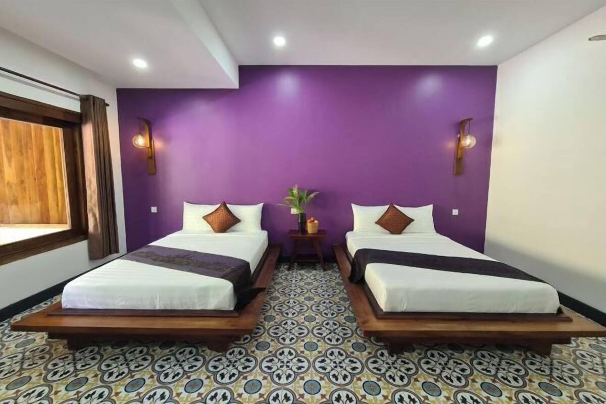 A room with two beds, purple walls, and patterned floor tiles.