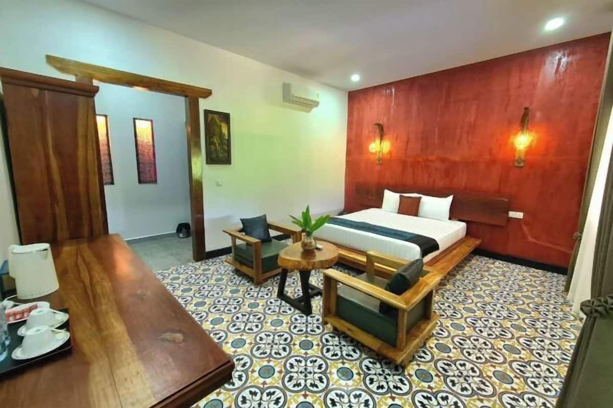 A hotel room with a bed, a wooden desk, a small table with chairs, and a patterned floor.