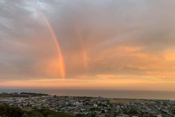 A coastal town with a view of the ocean and a rainbow in the sky. - 5 Bed Panoramic Sea & Town View (Oamaru)