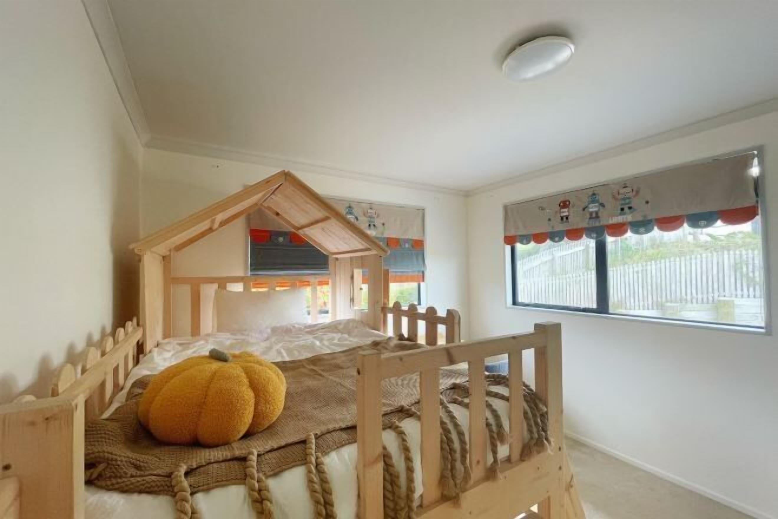 Una habitación infantil con una cama litera de madera, una decoración grande con forma de calabaza y una ventana que da a una cerca blanca.