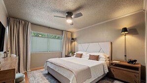 Un dormitorio con una cama grande, un escritorio, una silla, una mesita de noche, una lámpara y un ventilador de techo.