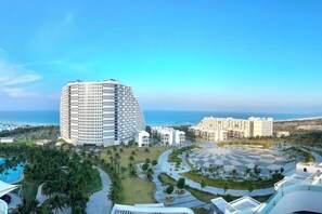 A modern hotel with a curved facade, a pool, and a view of the sea. - The Oceanfront Apartment At Cam Ranh (Cam Ranh)