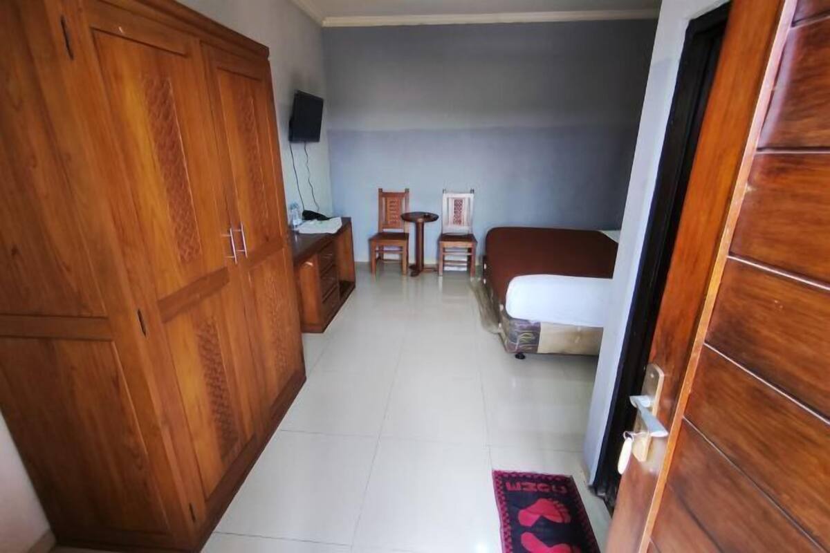 A hotel room with a wooden wardrobe, a bed, a small table with chairs, and a TV mounted on the wall.