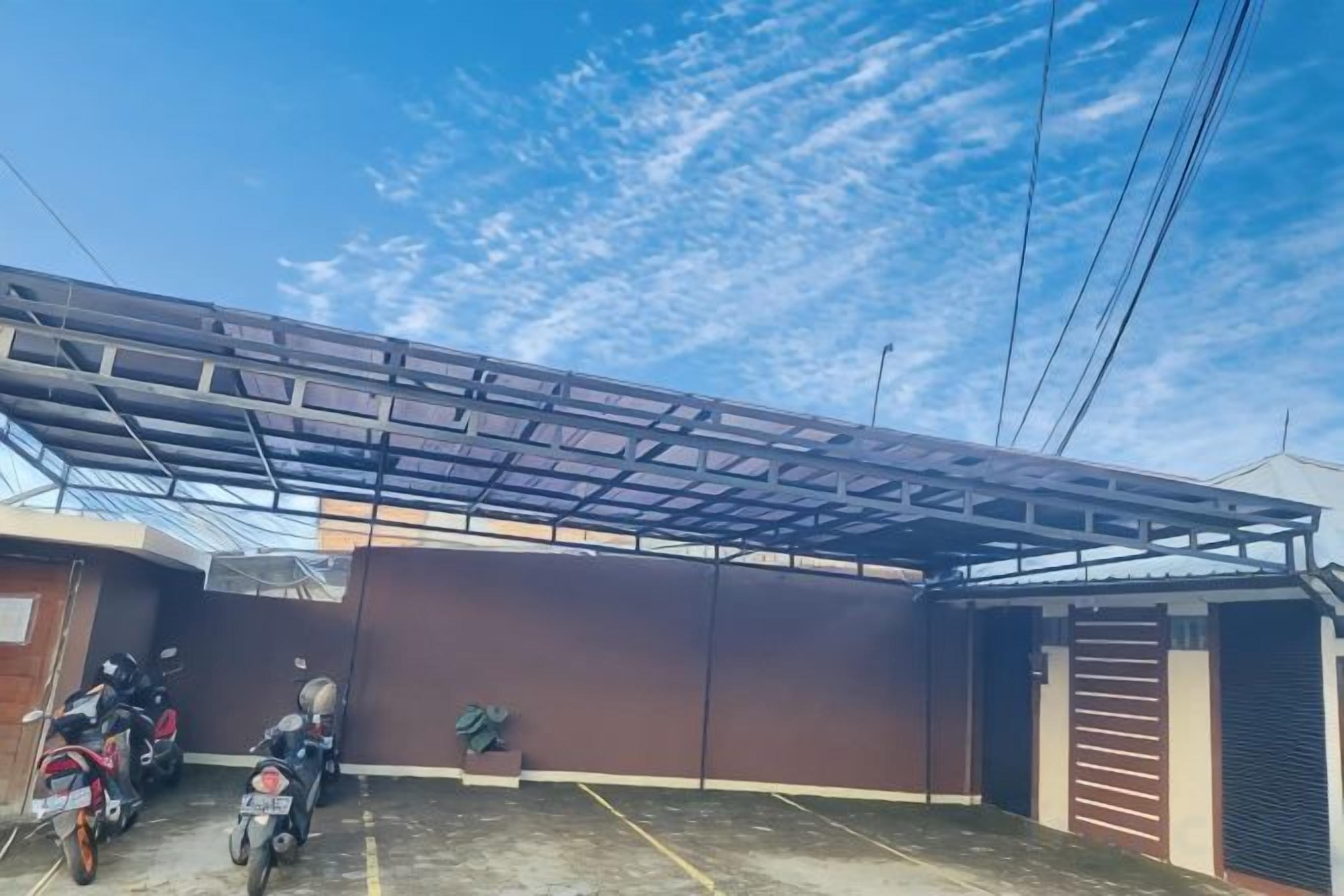 A covered outdoor area with a metal roof structure, a brown wall, and a motorcycle parked to the side.